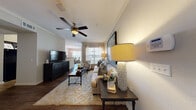 This single-floor residence offers a thoughtfully designed layout that balances comfort and functionality throughout. The living room serves as the heart of the home, featuring rich dark hardwood flooring, crown molding, a ceiling fan, and large windows dressed with sheer curtains and horizontal blinds that invite generous natural light. A plush neutral sofa, accent armchair, and a statement art piece create an inviting, cohesive aesthetic that flows seamlessly into the adjacent dining area, where a round dark-finished table is positioned beside a bright window overlooking the outdoors.

The kitchen is equipped with dark cabinetry, black appliances, and a granite-topped island that opens directly to the living space, making it ideal for both everyday use and entertaining. Two well-proportioned bedrooms each feature soft carpeting, ceiling fans, and windows with sheer curtains that fill the rooms with soft, diffused light. One bedroom showcases a neutral, contemporary palette while the other features warm, floral accents. The bathroom is finished with a granite vanity countertop, dark wood cabinetry, and a framed mirror, lending a clean and polished look. Throughout the residence, consistent finishes and warm lighting contribute to a cohesive and comfortable living environment.