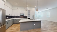 Located at 500 W Camelback Rd in Phoenix, AZ, this single-story home offers five bedrooms, two bathrooms, and a thoughtfully designed open floor plan. The heart of the home is a modern kitchen and living room combination that showcases light wood-tone flooring, recessed lighting, and pendant lights above a spacious central island with a white quartz countertop and built-in sink. Two-tone cabinetry pairs white upper cabinets with gray lower cabinets, accented by a dark subway tile backsplash. Stainless steel appliances, including a French door refrigerator, microwave, and range, complete the well-equipped kitchen. Open shelving adds functional display space. The living area flows naturally from the kitchen, bathed in natural light from multiple windows with horizontal blinds. An exterior door with a full-length sidelight window provides additional brightness. The five bedrooms feature plush neutral carpeting and windows that allow ample natural light. A dedicated walk-in closet with built-in rods and shelving serves the primary bedroom. The two bathrooms are finished with wood-tone flooring, a tub-shower combination, and clean white fixtures, offering a bright and functional design throughout.