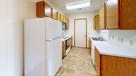 This single-floor unit offers a functional, well-organized layout with clearly defined living, sleeping, and kitchen zones. The living area features neutral wall-to-wall carpeting, warm wood baseboards, and a textured ceiling, creating a clean and adaptable space. A distinctive pass-through window with wood-trimmed cabinetry connects the living area to the kitchen, enhancing the sense of openness between the two spaces.

The galley-style kitchen is equipped with oak cabinetry extending to the ceiling for ample storage, white appliances including a full-size refrigerator and electric range, an over-range microwave, and a stainless steel sink. The flooring transitions to durable tile-style vinyl, and a door at the end of the kitchen provides additional access.

Multiple carpeted bedrooms each feature neutral tones, wood-trimmed windows with blinds that allow natural light, and textured ceilings with flush-mount lighting. The rooms offer generous wall space and are versatile in their potential use.

The bathroom includes an oak vanity with a wide white countertop, a large wall mirror, a toilet, and a walk-in shower with sliding glass doors. Overall, the unit maintains a consistent, neutral aesthetic throughout with warm wood accents providing cohesion.