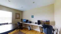 This single-floor business center offers a functional and well-organized workspace designed to support productivity. The room features a long, continuous white built-in desk that spans the width of the wall, providing ample surface area for two complete computer workstations. Each station is equipped with a desktop computer tower and monitor, allowing multiple users to work simultaneously. A shared printer and a telephone are also conveniently positioned along the desk, ensuring access to essential office equipment.

The space is finished with warm hardwood flooring that adds a welcoming touch to the otherwise utilitarian environment. The walls are painted in a soft, neutral tone, contributing to a calm and focused atmosphere. Recessed lighting in the white ceiling provides clean, even illumination throughout the room. A framed decorative artwork on one wall and a small potted plant add subtle character to the space without distracting from its primary purpose.

Ergonomic task chairs accompany each workstation, and a small waste bin is conveniently placed beneath the desk. An informational notice is posted on the wall, likely outlining usage guidelines. Overall, this business center is a practical and neatly maintained space suited for tasks such as printing, correspondence, and general computer use.