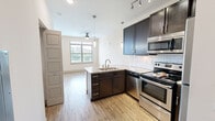 Located at 300 State St in downtown Knoxville, TN, this efficiently designed single-floor unit offers a thoughtful open-concept layout that maximizes every square foot. The combined kitchen and living area serves as the heart of the space, showcasing a well-appointed kitchen with dark espresso cabinetry, granite countertops, a subway tile backsplash, and a full suite of stainless steel appliances including a range, microwave, dishwasher, and refrigerator. A peninsula with an undermount sink and pendant lighting adds both functionality and style. Track and ceiling fan lighting throughout keeps the space bright and well-lit. The living area benefits from large windows with horizontal blinds and a set of glass-paneled French doors that invite abundant natural light and offer outdoor views. Light wood-style flooring flows seamlessly throughout the open-plan space, enhancing the airy feel. A dedicated closet houses a stacked washer and dryer unit, adding in-unit laundry convenience. The bathroom features large-format tile flooring, a dark vanity with granite countertop, and a subway-tiled tub and shower combination, maintaining the consistent modern aesthetic found throughout the unit.