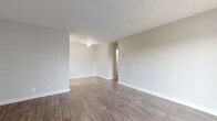 This single-floor residence offers a practical and well-organized layout, accommodating two bedrooms, three bathrooms, two kitchens, a living room, a hallway, and a closet. The living area is open and bright, featuring warm wood-style plank flooring, neutral beige walls, crisp white baseboards, and a textured ceiling with a ceiling fan — a combination that creates a clean, welcoming atmosphere. A sliding glass door dressed with vertical blinds allows natural light to filter in and provides access to the exterior. The kitchen is efficiently designed with white cabinetry, a marble-style countertop, a single-basin sink, and white appliances including a refrigerator and an electric range, all set against the same durable wood-style flooring. The bedrooms are comfortably sized, with the primary bedroom offering a built-in closet with sliding doors and a window dressed with vertical blinds that brings in outdoor light. The bathrooms feature white vanities topped with marble-style counters, mirrored medicine cabinets, and wood-style flooring, maintaining the cohesive aesthetic throughout. A bright hallway with open shelving connects the private areas of the home, completing a thoughtfully arranged floor plan.