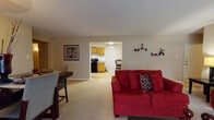 Located at 1108 Kennebec St. in Oxon Hill, Maryland, this single-floor residence offers a well-organized and comfortable layout designed for everyday living. The living room is a welcoming focal point, featuring plush carpeting, neutral-toned walls, and a large sliding glass door that frames outdoor greenery and fills the space with natural light. A large wall mirror enhances the sense of openness throughout the room. Adjacent to the living area, the dining space accommodates a full dining set beneath a decorative chandelier, with wall shelving adding a personalized touch. The kitchen is efficiently laid out with warm oak cabinetry, light granite-style countertops, tile flooring, and black appliances including a full-size refrigerator, electric range, and microwave. The bedrooms are carpeted and comfortably sized, each featuring windows that bring in natural light. One bedroom features a distinctive two-tone wall treatment with rich earth tones and a decorative modular shelf display, while another offers a more neutral palette with teal accent curtains. Throughout the residence, the consistent use of warm, neutral tones and carpet flooring creates a cohesive and inviting atmosphere.