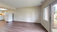 Located at 45 Thomas Olney Common in Providence, Rhode Island, this single-floor unit offers a practical and efficiently designed layout that includes a living room, kitchen, closet, and bathroom. Wood-style laminate flooring extends consistently throughout the space, lending a cohesive and clean aesthetic to every room.

The living area is open and simply appointed, featuring neutral beige walls, a side window, and a sliding glass door fitted with vertical blinds that provides direct outdoor access and brings in natural light with views of surrounding greenery. The straightforward layout makes the space adaptable for various furniture arrangements.

The kitchen is situated toward one end of the unit and features white cabinetry with ample upper and lower storage, dark laminate countertops, a single-basin sink, and a white gas range with an overhead ventilation hood. A pass-through counter connects the kitchen to the adjacent living area, enhancing the open feel.

The closet includes a full-width hanging rod and upper shelving, offering organized storage capacity. The bathroom is well-appointed with white tile surround, a tub-shower combination equipped with accessibility grab bars, a toilet, and a white vanity with sink. The overall ambiance throughout the unit is clean, neutral, and functional.