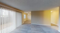 This single-floor residence offers a well-organized and functional layout designed for comfortable everyday living. The living area is generously sized, featuring soft wall-to-wall carpeting, warm neutral-toned walls, and a textured ceiling. Large sliding glass doors with vertical blinds flood the space with natural light and provide access to the outdoors, while a ceiling fan in the adjoining area adds both comfort and air circulation.

The galley-style kitchen is efficiently arranged with warm wood-toned cabinetry lining both sides, offering ample upper and lower storage. Gray laminate countertops provide practical workspace, complemented by a double basin sink, a white electric range, a refrigerator, and a dishwasher. Light vinyl flooring completes the kitchen's clean, functional aesthetic.

The two bedrooms are carpeted and well-lit by natural light through horizontal-blind windows. One bedroom features a walk-in closet with built-in shelving, providing excellent storage capacity.

The bathroom includes a full-size soaking tub with white tile surround and a grab bar for added accessibility. A separate vanity area features a wood-cabinet sink, large mirrors, bright vanity lighting, and convenient in-unit stacked laundry. The overall ambiance is clean, practical, and move-in ready.