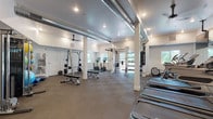 Located along East Lake Sammamish Parkway in Redmond, Washington, this fitness facility is thoughtfully designed to support a wide range of workout routines. The single-floor space features an open, expansive layout with white walls, exposed industrial-style ductwork running along the ceiling, and durable interlocking rubber tile flooring throughout—providing both functionality and a contemporary aesthetic.

The cardio zone is anchored by multiple treadmills positioned in front of large wall-mounted mirrors and a flat-screen television, enhancing the workout experience. Natural light filters in through several windows, keeping the environment bright and inviting. Ceiling fans complement the HVAC system, maintaining comfortable airflow.

The strength training area includes a power rack with a barbell and weight plates, adjustable benches, and a multi-functional cable machine. A well-organized rack displays a full set of kettlebells and dumbbells, allowing for versatile free-weight training. Stationary bikes with integrated screens, a wooden rowing machine, a punching bag, and a wall-mounted rig offer additional options for cardio and functional fitness.

A dedicated wall features a curated grid of framed abstract artwork, adding a polished, design-forward element to the space. Stability balls and accessories are neatly stored, rounding out the comprehensive equipment selection available throughout this well-appointed fitness center.