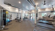 Located along East Lake Sammamish Parkway in Redmond, Washington, this fitness facility is thoughtfully designed to support a wide range of workout routines. The single-floor space features an open, expansive layout with white walls, exposed industrial-style ductwork running along the ceiling, and durable interlocking rubber tile flooring throughout—providing both functionality and a contemporary aesthetic.

The cardio zone is anchored by multiple treadmills positioned in front of large wall-mounted mirrors and a flat-screen television, enhancing the workout experience. Natural light filters in through several windows, keeping the environment bright and inviting. Ceiling fans complement the HVAC system, maintaining comfortable airflow.

The strength training area includes a power rack with a barbell and weight plates, adjustable benches, and a multi-functional cable machine. A well-organized rack displays a full set of kettlebells and dumbbells, allowing for versatile free-weight training. Stationary bikes with integrated screens, a wooden rowing machine, a punching bag, and a wall-mounted rig offer additional options for cardio and functional fitness.

A dedicated wall features a curated grid of framed abstract artwork, adding a polished, design-forward element to the space. Stability balls and accessories are neatly stored, rounding out the comprehensive equipment selection available throughout this well-appointed fitness center.