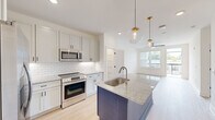Located at 455 51st St in Wilmington, NC, this thoughtfully designed one-bedroom, one-bathroom residence offers a clean, contemporary aesthetic throughout its efficiently organized single-floor layout. The open-concept living and kitchen area serves as the heart of the home, anchored by a striking navy blue kitchen island topped with speckled granite countertops and an undermount sink. White shaker-style cabinetry lines the walls above a classic subway tile backsplash, complemented by stainless steel appliances including a French door refrigerator, electric range, built-in microwave, and dishwasher. Globe pendant lights with gold accents hang above the island, adding a modern touch. Light hardwood-style flooring flows through the living area, which is brightened by large windows and a ceiling fan, with a glass door opening to a private balcony. The bedroom features plush carpeting, a ceiling fan, and a dedicated window that invites natural light. A separate closet provides ample storage. The bathroom includes a full tub and shower combination with oil-rubbed bronze fixtures. A dedicated laundry room houses a full-size, top-loading washer and dryer, adding everyday convenience to this well-appointed Wilmington residence.
