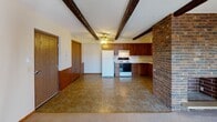 This single-floor unit offers a well-defined layout with a variety of distinctive architectural details throughout. The spacious living room is immediately eye-catching, featuring dark wood ceiling beams set against a textured ceiling, with neutral carpet underfoot. A door leads directly to a private balcony, allowing natural light to fill the room through a glass-paneled entry and a vertical blind-covered window. Baseboard heating runs along the perimeter, ensuring efficient climate control.

The kitchen is equipped with rich, warm-toned wood cabinetry that wraps around the room in an L-shape, complemented by tile flooring and a ceiling fan with light fixture overhead. A full suite of white appliances — including a refrigerator, electric range, and dishwasher — is integrated into the cabinetry. A partial exposed brick accent wall adds a rustic touch at the kitchen's edge, alongside wood wall paneling near the entryway.

Two carpeted bedrooms provide comfortable, quiet retreats, each featuring windows with wood-trimmed frames and baseboard heating. The full bathroom includes small-format mosaic tile flooring, white wall tile with a contrasting border, a wood vanity with a stone-patterned countertop, and a drop ceiling. The overall ambiance of the unit is practical and functional, with warm, earthy tones tying each room together.