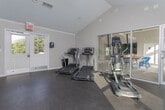 Located in Acworth, Georgia, this single-floor community clubhouse at 4801 Baker Grove Rd NW offers a thoughtfully designed gathering space that blends modern aesthetics with warm, inviting details. The main lounge area immediately draws attention with a dramatic diagonal reclaimed wood accent wall, serving as a bold focal point behind the wall-mounted television. Plush carpeting, a ceiling fan, and a coffered tray ceiling add comfort and architectural refinement to the space, while a large arched window floods the room with natural light and provides views of the surrounding neighborhood.

The open-concept layout flows seamlessly from the lounge into a casual dining area, where a generously sized farmhouse-style dining table surrounded by navy Windsor chairs sits beneath another tray ceiling with a ceiling fan. Multiple arched windows and a glass door frame picturesque views of the outdoor pool, allowing abundant sunlight to pour in throughout the day.

Adjacent to the lounge, a bar area features sleek bar-height seating and a striking emerald green subway tile backsplash, creating a vibrant contrast against the otherwise neutral palette. The overall ambiance is clean, contemporary, and welcoming — designed to serve as an ideal social hub for the community.