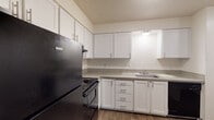Located at 9705 SW Hall Blvd in Portland, Oregon, this single-floor unit offers a practical and comfortable layout designed for everyday living. The kitchen is a standout feature, equipped with black appliances including a refrigerator, electric range, and dishwasher. White shaker-style cabinetry with bar-pull hardware lines the walls, providing generous storage, while granite-look countertops and a stainless steel sink add a clean, functional aesthetic. Wood-style plank flooring runs throughout the kitchen and living areas, lending warmth and easy maintenance. The open living area connects seamlessly to the kitchen via a pass-through window, enhancing the sense of openness. A sliding glass door leads to a private balcony, allowing natural light to fill the space and offering outdoor access. The bedrooms feature plush carpeting and windows that bring in natural light, with baseboard heating ensuring year-round comfort. Neutral wall tones throughout create a versatile canvas. The bathroom includes a full tub and shower surround in a clean white finish. Textured ceilings are present throughout the unit, consistent with the building's design character.