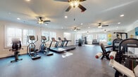 The Blakely's fitness center is a generously proportioned, single-level facility designed to support a comprehensive workout experience. The space is finished with durable rubber flooring throughout the main exercise areas, providing both comfort and functionality for a wide range of activities.

The cardio zone is outfitted with multiple treadmills and elliptical machines, positioned to take full advantage of the abundant natural light streaming through large windows along the perimeter walls. These windows also offer views of the surrounding community, creating an open and inviting atmosphere during workouts.

Strength training is well represented, with a cable machine and several selectorized weight stations distributed across the floor. A dedicated free weight area includes a full rack of dumbbells, while stability balls and additional accessories are neatly organized for functional and group fitness use.

Large wall-mounted mirrors in the strength training section enhance the sense of space and allow users to monitor their form. Multiple ceiling fans are installed throughout, ensuring consistent airflow and comfort. Recessed lighting and crown molding details contribute a polished, refined aesthetic to the space.

The facility's layout supports simultaneous use across multiple zones — cardio, strength, and stretching — making it a versatile and well-rounded amenity for residents of The Blakely.