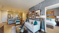 This single-floor residence showcases a thoughtfully designed open-concept layout that seamlessly connects the living, dining, and kitchen areas. The living room is a standout space, anchored by a striking textured accent wall with an industrial, concrete-like finish that serves as a backdrop for a curated gallery of framed artwork. Large windows allow generous natural light to fill the room, complementing the warm hardwood-style flooring that extends throughout the main areas.

The kitchen is well-appointed with wood-tone cabinetry extending to the ceiling, granite countertops, a full suite of stainless steel appliances, a subway tile backsplash, and a large island with seating — ideal for casual dining. Pendant lighting adds a refined touch overhead.

Both bedrooms are comfortably scaled, featuring plush carpeting, large windows with ample natural light, and easy access to their respective bathrooms. Each bathroom is finished with wood-tone vanities, granite countertops, hardwood-style flooring, and a tub-shower combination. One bedroom includes a walk-in closet area with built-in shelving. The overall ambiance is modern and cohesive, with neutral tones and contemporary finishes creating a polished, move-in-ready feel throughout.