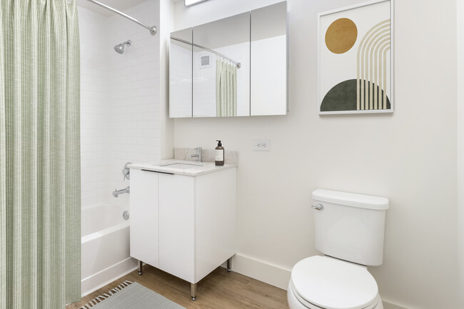 Renovated Package I bath with white marbled quartz countertops, white cabinetry, and hard surface flooring - Avalon Morningside Park