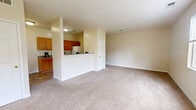 This single-floor, 1-bedroom, 1-bathroom residence offers a thoughtfully designed layout that maximizes both comfort and functionality. The open living area features neutral-toned carpet, warm beige walls, and multiple windows that flood the space with natural light while providing pleasant views of the surrounding greenery. A glass-panel exterior door further connects the living space to the outdoors.

The galley-style kitchen is efficiently designed, featuring warm wood cabinetry, grey laminate countertops, tile flooring, and a full suite of white appliances including a range, refrigerator, and dishwasher. A breakfast bar-style peninsula separates the kitchen from the living area, creating a natural transition between spaces.

The carpeted bedroom is a comfortable size, benefiting from a large window that brings in ample natural light and offers views of the open landscape outside. A carpeted hallway connects the bedroom to the rest of the unit, providing a sense of defined separation between spaces.

The bathroom includes a tiled tub-shower combination, a wooden vanity with a white countertop, and warm stone-look tile flooring. A dedicated laundry room offers wire shelving, washer/dryer hookups, and additional storage potential, rounding out this practical and well-organized residence.