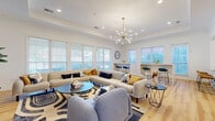 Located at 2594 Chestnut Oak Way in Columbus, Ohio, this single-floor space offers a thoughtfully designed open-concept layout that seamlessly connects the living and kitchen areas. Light hardwood flooring runs throughout, creating a warm, cohesive foundation that ties the entire space together.

The living area is bright and inviting, with large windows fitted with white blinds that allow generous natural light to fill the room. A tray ceiling with crown molding adds architectural dimension, while a striking sputnik chandelier with a brass finish serves as a central design statement. A slatted wood accent wall anchors the entertainment zone, providing a modern, textural backdrop.

The kitchen is clean and functional, featuring white shaker-style cabinetry with matte black hardware, granite countertops with subtle veining, and a stainless steel refrigerator. A peninsula with bar seating provides additional workspace and casual dining options, while a window above the sink introduces natural light into the cooking area.

Adjacent to the living space, a dedicated bar-height communal table with teal upholstered stools offers a versatile area for dining or gathering. Multiple windows surround this zone, enhancing the airy atmosphere. Throughout the space, white walls, recessed lighting, and carefully chosen decor contribute to a modern, welcoming ambiance.