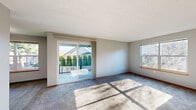 Located at 6601 Hidden Creek Loop NE in Keizer, Oregon, this single-story, 2-bedroom, 1-bathroom home offers a practical and comfortable layout. The living room is a standout space, featuring plush carpeting, neutral gray walls, and abundant natural light streaming through dual windows and a sliding glass door that opens to an outdoor balcony area with views of neighboring greenery and mature trees. The kitchen is efficiently designed with warm honey-toned wood cabinetry, gray laminate countertops, a white refrigerator, and an electric range. Light wood-style vinyl flooring runs throughout the kitchen, which connects to a bright dining nook with a window view. The primary bedroom is generously sized, offering carpeted flooring, neutral wall tones, and a window that fills the room with natural light. The second bedroom features carpet, a closet with sliding wood doors and built-in rod storage, and a wall-mounted heating unit. Both bedrooms are finished with warm wood baseboards. The full bathroom includes a wood-toned vanity with a gray countertop, a tub/shower combo, and light wood-style flooring. Throughout the home, consistent finishes including gray walls, wood-toned trim, and textured ceilings create a cohesive and functional living environment.