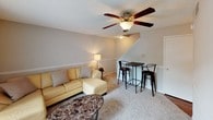 This two-floor home at Well 22 offers a well-organized layout designed for comfortable everyday living. The main level features a carpeted living room with a ceiling fan, a sliding glass door that opens to an outdoor balcony, and plenty of natural light. A dining bar area with seating sits conveniently beside the staircase, making the space ideal for casual meals or gatherings. The kitchen is efficiently designed with warm wood cabinetry, dark granite-style countertops, hardwood-style flooring, and a window that lets in natural light. It is equipped with a gas range, dishwasher, and full-size refrigerator. The upper floor houses multiple bedrooms, each carpeted and featuring windows with blinds for natural light and privacy. The bedrooms include closet space and offer a quiet, comfortable retreat. A shared hallway on the upper level provides access to a linen or utility closet with louvered doors. The bathroom is clean and straightforward, featuring a white vanity with cabinetry, a mirror, a three-bulb vanity light fixture, and hardwood-style flooring. Neutral tones are carried throughout the home, creating a cohesive and understated aesthetic across both floors.