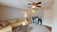 This two-floor home at Well 22 offers a well-organized layout designed for comfortable everyday living. The main level features a carpeted living room with a ceiling fan, a sliding glass door that opens to an outdoor balcony, and plenty of natural light. A dining bar area with seating sits conveniently beside the staircase, making the space ideal for casual meals or gatherings. The kitchen is efficiently designed with warm wood cabinetry, dark granite-style countertops, hardwood-style flooring, and a window that lets in natural light. It is equipped with a gas range, dishwasher, and full-size refrigerator. The upper floor houses multiple bedrooms, each carpeted and featuring windows with blinds for natural light and privacy. The bedrooms include closet space and offer a quiet, comfortable retreat. A shared hallway on the upper level provides access to a linen or utility closet with louvered doors. The bathroom is clean and straightforward, featuring a white vanity with cabinetry, a mirror, a three-bulb vanity light fixture, and hardwood-style flooring. Neutral tones are carried throughout the home, creating a cohesive and understated aesthetic across both floors.