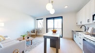 This thoughtfully designed single-floor residence combines modern aesthetics with functional living across a well-appointed layout. The open-concept living and dining area serves as the heart of the home, anchored by light-toned hardwood flooring that flows throughout. A sleek island with a white countertop defines the transition between the kitchen and living space, illuminated by a striking dual-globe pendant light fixture with a brass accent. Large black-framed windows and a sliding glass door flood the area with natural light while providing direct access to a private balcony with outdoor views.

The kitchen is outfitted with crisp white shaker cabinetry, a classic subway tile backsplash, and stainless steel appliances including a range, over-the-range microwave, and dishwasher. A standout stainless steel farmhouse sink with a matte black faucet adds a refined, contemporary touch.

The living area is open and airy, comfortably accommodating a seating arrangement centered around a mid-century modern coffee table. The bedroom offers a calm, neutral retreat with soft carpeting, warm ambient lighting, and generous closet space. The bathroom features a white vanity with shaker-style cabinetry, a matte black faucet, an integrated sink, and a large wall mirror, delivering a clean and modern finish throughout.