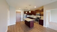 This single-floor unit offers a thoughtfully designed layout with contemporary finishes throughout. The kitchen serves as a central highlight, showcasing rich dark cabinetry, granite countertops, a center island with additional granite surface space, and a full suite of stainless steel appliances including a refrigerator, electric range, microwave, and dishwasher. Warm hardwood-style flooring and elegant pendant lighting complete the kitchen's polished aesthetic.

The unit features two generously sized bedrooms, both finished with plush neutral carpeting and windows that allow natural light to fill the space while offering views of the surrounding neighborhood. One bedroom connects directly to a walk-in closet equipped with wire shelving, providing ample storage, and provides convenient access to a full bathroom.

Both bathrooms are well-appointed, each featuring a shower-tub combination with a curved curtain rod, a toilet, and a vanity with granite countertops and dark wood cabinetry. The neutral, warm-toned walls throughout the unit create a cohesive and calming ambiance.

The overall design balances modern finishes with functional living spaces, making this a comfortable and stylish residence suited for everyday living.