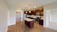 This single-floor unit offers a thoughtfully designed layout with contemporary finishes throughout. The kitchen serves as a central highlight, showcasing rich dark cabinetry, granite countertops, a center island with additional granite surface space, and a full suite of stainless steel appliances including a refrigerator, electric range, microwave, and dishwasher. Warm hardwood-style flooring and elegant pendant lighting complete the kitchen's polished aesthetic.

The unit features two generously sized bedrooms, both finished with plush neutral carpeting and windows that allow natural light to fill the space while offering views of the surrounding neighborhood. One bedroom connects directly to a walk-in closet equipped with wire shelving, providing ample storage, and provides convenient access to a full bathroom.

Both bathrooms are well-appointed, each featuring a shower-tub combination with a curved curtain rod, a toilet, and a vanity with granite countertops and dark wood cabinetry. The neutral, warm-toned walls throughout the unit create a cohesive and calming ambiance.

The overall design balances modern finishes with functional living spaces, making this a comfortable and stylish residence suited for everyday living.