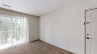This single-floor unit is designed with a functional, straightforward layout that maximizes usability across its various spaces. The living area is finished with wall-to-wall carpet in a warm neutral tone and receives natural light through a large window fitted with vertical blinds. A front entry door opens directly into this open living space, which connects to the kitchen via a peninsula counter with a built-in sink, creating a natural division between the two areas.

The galley-style kitchen is efficiently arranged with light wood cabinetry lining both walls, offering ample upper and lower storage. Countertops in a neutral laminate finish run the length of both sides, accompanied by a double basin sink, a gas range with overhead ventilation, a dishwasher, and a full-size refrigerator. Stone-look tile flooring completes the kitchen and extends into the bathrooms.

The bedrooms are carpeted and well-proportioned, each with vertical blinds on the windows. One bedroom includes a ceiling fan and a double-door closet. Both bathrooms feature tub and shower combinations, tile flooring, a vanity with storage, and clean white fixtures throughout.
