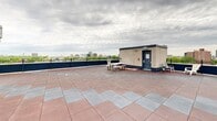 Located atop a building in the heart of Montréal, this rooftop terrace at 3777 Rue Saint-Urbain offers an impressive open-air retreat with sweeping panoramic views of the city skyline, lush treetops, and iconic landmarks including a glimpse of Mont-Royal. The terrace is laid with a durable two-tone tile pattern in alternating red and grey, covering a generously sized L-shaped footprint that wraps around a central brick mechanical enclosure. Sturdy ornamental dark metal railings line the perimeter, providing both safety and an unobstructed view of the surrounding cityscape. The space is well-suited for outdoor gathering and relaxation, with seating areas that include a bistro table and chairs as well as a picnic bench positioned to take full advantage of the views. Sliding glass doors connect one section of the terrace to the building interior, adding convenience and accessibility. The brick facade of the rooftop structure adds a classic architectural character that contrasts with the modern tile underfoot. With open sightlines in multiple directions, the terrace captures the vibrant energy of the Plateau-Mont-Royal neighbourhood, making it a distinctive and functional outdoor amenity.