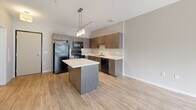 Located at 6730 Cedar Ave S in Richfield, MN, this one-bedroom, one-bathroom unit delivers a well-designed, efficient floor plan with modern finishes throughout. The open-concept living and kitchen area is anchored by a sleek kitchen island with a white quartz-style countertop, illuminated by a contemporary pendant light fixture. The kitchen features dark wood-grain cabinetry extending to the ceiling, providing ample storage, complemented by white countertops, a stainless steel sink, and black appliances including a refrigerator, range, microwave, and dishwasher. Light wood-look flooring runs throughout the main living area, enhancing the bright and airy atmosphere. Large sliding glass doors lead to a private balcony, allowing natural light to flood the space and offering outdoor views. The bedroom is a comfortable, carpeted retreat with a large window that brings in additional natural light and is paired with a dedicated closet for storage. The bathroom is clean and functional, featuring a full soaking tub and shower combination with chrome fixtures and crisp white surround. Track lighting in the kitchen and neutral tones throughout create a cohesive, contemporary aesthetic suited for modern living.