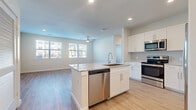 This thoughtfully designed single-floor residence offers a bright and modern living experience across a comfortable footprint. Light wood-style flooring flows seamlessly throughout every room, creating a cohesive and airy aesthetic.

The open-concept kitchen serves as the centerpiece of the home, featuring a large central island with a granite countertop and an undermount sink with a stainless steel dishwasher below. White shaker-style cabinetry lines the walls, complemented by a subway tile backsplash and a full suite of stainless steel appliances including a French door refrigerator, electric range, and over-the-range microwave.

The kitchen opens directly into the living room, which is bathed in natural light from a pair of large windows fitted with white blinds. A ceiling fan overhead adds both function and style to the space.

The bedroom is a well-sized, serene retreat with its own window and ceiling fan, offering ample natural light and ventilation. It provides access to a dedicated walk-in closet equipped with multi-tiered wire shelving for generous storage.

The bathroom is elegantly finished with a granite-topped white vanity, a large mirror, and a tub-shower combination surrounded by marble-style porcelain tile. Wood-look flooring continues into this space, tying the design together cohesively.