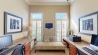 Located at 500 Carlen Ave in Lexington, South Carolina, this single-room office is a thoughtfully designed workspace that balances functionality with refined aesthetics. The room features notably tall ceilings accentuated by decorative crown molding, lending an open and airy atmosphere throughout. Two large windows fitted with classic plantation shutters and transom windows above flood the space with generous natural light, creating a bright and welcoming environment.

Built-in granite-topped workstations with warm cherry wood cabinetry and drawers line two walls of the office, providing ample workspace and storage for multiple users. Desktop computers and a printer are integrated seamlessly into the setup, making this a fully operational business center. A cushioned bench seat positioned centrally between the workstations offers a comfortable waiting or collaborative area. Framed artwork adorns the walls, contributing to the polished, professional ambiance.

Neutral warm beige tones on the walls complement the rich wood finishes and granite surfaces, creating a cohesive and inviting interior palette. Soft carpeting underfoot adds comfort to the workspace. A doorway leads to an adjacent alcove featuring a water fountain, enhancing the convenience of the space. This office is a well-equipped, elegantly finished environment suited for productive and professional use.