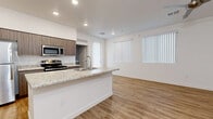 Located at 13404 N 30th Ave in Phoenix, Arizona, this well-designed 2-bedroom, 2-bathroom residence offers a clean, contemporary aesthetic across a single-floor, efficiently planned layout. The open-concept living and kitchen area serves as the heart of the home, anchored by a central island with granite-style countertops and an integrated sink. The kitchen is fully equipped with stainless steel appliances, including a refrigerator, electric range, microwave, and dishwasher, complemented by warm-toned cabinetry. Recessed lighting illuminates the space, while large windows fitted with vertical blinds allow ample natural light into the living area. Consistent warm-toned wood-look flooring flows throughout the entire residence, creating a cohesive and inviting atmosphere. The primary bedroom features elevated ceilings, a ceiling fan, a window for natural light, and direct access to its own bathroom. The second bedroom is bright and well-proportioned, offering a sliding-door closet with built-in shelving. Both bathrooms are finished with wood-toned vanity cabinetry, granite-style countertops, and a shower-tub combination enclosed by sliding glass doors. Clean white walls and modern panel-style doors complete the polished, move-in-ready presentation throughout the home.