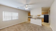 This single-floor, 2-bedroom, 2-bathroom unit in Lafayette, Louisiana offers a functional and practical layout designed to maximize its living space. The open-concept living and dining area is finished with neutral-toned carpet and features vaulted ceilings with a ceiling fan and light fixture, lending the space a sense of openness. A window along the exterior wall allows natural light to fill the room.

The kitchen is positioned adjacent to the living area and separated by a peninsula-style breakfast bar with dark granite-look countertops and decorative corbels — a practical feature that also enhances the flow between spaces. The kitchen is equipped with honey-toned wood cabinetry, matching dark granite countertops, tile flooring, and black appliances including a gas range, over-the-range microwave, and refrigerator.

Both bedrooms are carpeted and feature ceiling fans with light kits, windows with blinds, and neutral beige walls. The primary bedroom is generously proportioned and includes closet access. The secondary bedroom is comparably sized and similarly appointed.

Each of the two bathrooms is finished with tile flooring, a full tub-shower combination with a curved curtain rod, and dark granite-topped vanities — maintaining a consistent aesthetic throughout the unit.