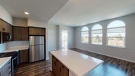 This single-floor unit showcases a thoughtfully designed open-concept layout that seamlessly connects the kitchen, dining, and living areas. Dark hardwood-style flooring runs consistently throughout, creating a warm, cohesive aesthetic that contrasts elegantly with the light grey walls and white trim.

The kitchen is a standout feature, equipped with stainless steel appliances including a gas range, built-in microwave, dishwasher, and refrigerator. Wood-toned cabinetry with matte black hardware pairs with white quartz countertops and a subway tile backsplash, lending a clean, modern character. A central island provides additional prep and storage space.

The living and dining area is bathed in natural light through a distinctive trio of arched windows, offering broad outdoor views and an airy atmosphere. A private exterior door connects the living space to an outdoor area, further enhancing the sense of openness.

Hallways connecting the rooms are well-proportioned, featuring recessed lighting and consistent flooring. Two bathrooms maintain the unit's modern aesthetic, each offering tub-shower combinations with tiled surrounds, wood-toned vanities, and white countertops.

Throughout the unit, clean lines, neutral tones, and consistent material choices create a polished, move-in-ready environment suited for contemporary living.