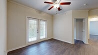 This single-story space is designed with a consistent aesthetic throughout, highlighted by wood-style flooring that runs across the living areas, bedrooms, and bathroom. The living room serves as a welcoming centerpiece, featuring crown molding, a ceiling fan with a light fixture, and a pair of French doors fitted with blinds that invite natural light and provide views of surrounding greenery.

The kitchen is thoughtfully laid out with warm-toned wooden cabinetry, granite-style countertops, and a peninsula that separates it from the adjoining living space. White appliances, including a range, microwave, and refrigerator, are integrated into the cabinetry, and a double-door pantry or storage closet provides additional organization. A sink with a window view adds functionality to the workspace.

The bedrooms are generously proportioned, each featuring wood-style flooring, neutral walls, and windows with blinds that frame views of outdoor greenery. Ceiling fans are present in select rooms. At least one bedroom includes a walk-in closet with built-in shelving and rod storage.

The bathroom offers a wide vanity with an extended countertop, white cabinetry, a large mirror, and a separate shower area. The neutral color palette and consistent flooring maintain a cohesive, clean ambiance throughout the entire space.