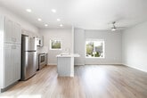 This thoughtfully designed two-story home offers 2 bedrooms and 3 bathrooms across two well-proportioned floors. The main level features an open-concept kitchen and living area bathed in natural light from multiple windows. The kitchen is equipped with stainless steel appliances — including a refrigerator, range, and microwave — complemented by gray shaker-style cabinetry, white quartz countertops, and a central island with a built-in sink. Light hardwood flooring flows throughout the main level, and a ceiling fan anchors the airy living space. A dedicated laundry area with side-by-side washer and dryer adds everyday convenience. The upper floor houses both bedrooms, each finished with plush carpet and windows offering views of the surrounding greenery. The primary bedroom is generously sized and features a vaulted ceiling that adds a striking sense of height. Three bathrooms serve the home — one with a tub/shower combo and another with a glass-enclosed walk-in shower — each outfitted with white shaker vanities and warm hardwood-style flooring. A hallway, staircase, and closet round out the layout, providing functional flow throughout this clean, contemporary residence.