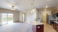 Located at 1803 Moon Meadows Dr in Rapid City, South Dakota, this two-bedroom, one-bathroom unit offers a well-designed single-level layout with a comfortable footprint. The open-concept living and dining area features plush carpeting and a ceiling fan, creating a relaxed, airy atmosphere. Sliding glass doors lead to a private balcony with an open railing, offering unobstructed views of the surrounding grasslands and distant hills.

The kitchen is well-appointed with rich dark cabinetry, granite countertops, a subway tile backsplash, and stainless steel appliances including a refrigerator, range, and built-in microwave. A peninsula with pendant lighting and an integrated sink connects the kitchen to the main living space.

Both bedrooms are carpeted and equipped with ceiling fans. The primary bedroom includes a walk-in closet featuring wire shelving for organized storage. The second bedroom offers a window with pleasant outdoor views. The full bathroom features a granite-topped vanity with dark wood cabinetry, a tub-shower combination with decorative tile accenting, and tile flooring. The overall aesthetic is clean and consistent throughout.