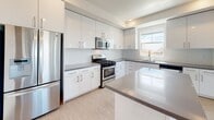 This single-floor residence in Folsom, California (95630) offers a clean, contemporary design throughout its well-organized layout. The kitchen serves as a central highlight, featuring bright white cabinetry extending to the ceiling, gray stone-look countertops, a subway tile backsplash, and a full suite of stainless steel appliances including a gas range, over-the-range microwave, refrigerator, and dishwasher. A central island provides additional counter space and casual seating. Light wood-look flooring runs through the kitchen and main living areas, contributing to the home's airy, modern aesthetic.

The living area is bright and open, flowing naturally from the kitchen, and features a sliding glass door that leads to a private balcony with open views of the surrounding neighborhood and hills. Natural light fills the space through multiple windows.

Bedrooms are carpeted for comfort and include sliding or paneled closet doors with built-in hanging rods. The bathrooms feature white cabinetry with gray countertops, large mirrors, tile flooring, and a combination tub and shower with white tile surround. The overall design is cohesive, neutral, and move-in ready.