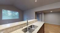 This single-floor unit showcases a thoughtfully designed open layout with vaulted ceilings that enhance the sense of space in the main living area. Track lighting illuminates the living room, which features light hardwood-style flooring and a large sliding glass door that floods the space with natural light and provides outdoor views. The open-plan kitchen is equipped with dark espresso cabinetry, granite countertops, and a full suite of stainless steel appliances, including a refrigerator, range, and microwave. A raised breakfast bar separates the kitchen from the living area, creating a natural flow between spaces.

The bedrooms are carpeted for comfort, each featuring windows with blinds that invite natural light. One bedroom includes a walk-in closet with built-in shelving, while another features a standard closet. A dedicated bathroom offers a granite-topped vanity with dark cabinetry and a large mirror with overhead lighting. A convenient in-unit stacked washer and dryer is tucked into a closet accessible from the bathroom hallway. Neutral gray and beige tones throughout lend the space a clean, contemporary aesthetic.
