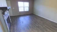 This single-floor space presents a straightforward and functional layout designed with practicality in mind. The interior is finished with rich, dark hardwood-style flooring that runs throughout, providing a grounded and cohesive aesthetic that pairs well with the neutral, warm-gray wall tones found across the space. The clean lines of the baseboards and trim add a subtle, polished finish to the rooms.

Natural light plays a notable role in the ambiance of the space. A large, multi-pane window allows daylight to flow generously into the main room, brightening the interior and creating an open, airy feel despite the understated color palette. The window also offers views of the surrounding exterior environment.

The overall atmosphere of the space is clean, minimal, and move-in ready, with no extraneous detail to distract from its core functional design. The dark flooring contrasts effectively against the lighter walls, adding visual depth and warmth to each room. The layout reflects a no-frills approach that prioritizes usability and comfort, making it well-suited for a variety of occupancy needs. The space is presented in a well-maintained condition throughout.