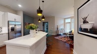 Located in the heart of Nashville, Tennessee, this well-appointed single-floor residence at 900 Third Ave N blends contemporary design with warm, inviting finishes. The open-concept living and kitchen area serves as the centerpiece of the home, where rich hardwood flooring flows seamlessly throughout. The kitchen is outfitted with crisp white cabinetry, stainless steel appliances, a decorative patterned tile backsplash, and a generous island with a white quartz countertop — topped by striking black pendant lights with gold interiors that add a bold design accent. The living room benefits from tall windows and a private entry door that usher in abundant natural light, complemented by a vaulted ceiling detail and a cozy, eclectic aesthetic. A dedicated dining area adjoins the living space, offering a natural transition toward the bedrooms. The bedrooms feature plush carpeting, large windows, teal accent walls, and pendant lighting. Both bathrooms are finished with white shaker-style vanities, black matte hardware, white quartz countertops, and classic black-and-white mosaic tile flooring, providing a clean and modern feel. Overall, the space exudes a curated, design-forward ambiance suited to urban Nashville living.