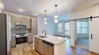 Located at 3238 Hidden Forest Ct in Marietta, GA, this thoughtfully designed one-bedroom, one-bathroom residence offers a modern aesthetic with high-quality finishes across its single-floor layout. The open-concept living, dining, and kitchen area serves as the heart of the home, anchored by a central island topped with granite countertops and a black matte faucet. The kitchen is outfitted with light wood cabinetry, a gray subway tile backsplash, and a full suite of stainless steel appliances, including a French door refrigerator, electric range, microwave, and dishwasher. Pendant lighting above the island adds a contemporary touch. Wood-look flooring flows through the main living areas, where natural light enters through windows and a glass-panel door that opens to a private outdoor space. A sliding barn door adds an architectural accent to the interior. The bedroom features plush carpet flooring, a ceiling fan, and a window with exterior views. The bathroom is finished with a granite-topped vanity with light wood cabinetry, a framed mirror, and a tiled walk-in shower, complemented by an adjacent closet with built-in shelving for organized storage.