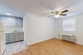 Located at 815 W Buford St in Gaffney, South Carolina, this single-floor unit offers a practical and efficiently designed layout encompassing one bedroom, one bathroom, a living room, and a kitchen. The living area is finished with warm wood-look laminate flooring, crown molding, and a ceiling fan with light fixture, creating a clean and comfortable atmosphere. Two windows allow natural light to fill the space, while a wall-mounted HVAC unit provides climate control. The kitchen is positioned adjacent to the living area and features gray cabinetry, a granite-style countertop, a sink, and white appliances including a refrigerator and range, making efficient use of the available space. The bedroom is carpeted for comfort and includes crown molding, a ceiling fan, a closet with built-in shelving, and a window with blinds for natural light. The full bathroom is finished with large-format neutral tile surrounding the tub-shower combination, complemented by a white vanity and a framed mirror. Throughout the unit, textured ceilings and white walls maintain a bright, consistent aesthetic, making this a straightforward and functional living space in Gaffney, SC.