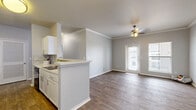 This single-story, 2-bedroom, 2-bathroom home offers a thoughtfully designed layout that maximizes comfort and functionality. The open-concept living and kitchen area serves as the heart of the home, featuring warm wood-look flooring, crown molding, and a ceiling fan. Natural light pours in through multiple windows and a glass-paneled front door, creating a bright and welcoming atmosphere. The kitchen is well-equipped with white cabinetry, a stone tile backsplash, light countertops, and black appliances, including a range, microwave, and dishwasher. A peninsula with a built-in sink connects the kitchen to the living area, enhancing the open flow of the space. A hallway lined with wood-look flooring and a ceiling-mounted light fixture connects the main living area to the private quarters. Both bedrooms are carpeted and generously sized, with the primary bedroom featuring dual corner windows that let in ample natural light and a ceiling fan overhead. The second bedroom offers wood-look flooring. Each bathroom is clean and functional, featuring white vanities with light countertops, a tub-shower combination, and wood-look flooring. A dedicated closet and hallway round out the layout, providing practical storage and ease of movement throughout the home.