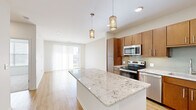 Located in Leawood, Kansas, this well-appointed 1-bedroom, 1-bathroom residence offers a thoughtfully designed open-concept layout. The kitchen serves as a central highlight, featuring rich warm-toned wood cabinetry, a full suite of stainless steel appliances, a glass tile backsplash, and an expansive granite-topped island with pendant lighting overhead — ideal for both meal prep and casual dining. Light wood-style flooring flows throughout the main living areas, enhancing the bright, airy atmosphere created by recessed lighting and large windows.

The living room is generously sized, bathed in natural light from a sliding glass door that opens to a private balcony overlooking a green outdoor landscape. The bedroom offers plush carpeting, a ceiling fan, and a dedicated window with blinds for natural light and privacy. A walk-in closet provides practical storage. The bathroom is finished with large-format tile flooring, a tiled soaking tub surround, and a wood-cabinet vanity with granite countertop, maintaining the cohesive design language found throughout the space. Clean white walls and neutral tones lend a modern, move-in-ready aesthetic throughout the entire residence.
