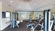 This fitness center offers a comprehensive and well-appointed workout environment designed to meet a variety of exercise needs. The space is anchored by a selection of strength training machines and adjustable benches, providing users with options for both resistance training and targeted muscle work. The rubber flooring throughout ensures safety and durability during high-intensity exercise.

A defining architectural feature is the octagonal coffered ceiling, which adds a refined, elevated aesthetic uncommon in typical gym settings. Recessed lighting is thoughtfully integrated into the ceiling, providing bright, even illumination throughout the space. Full-length mirror panels line one wall, enhancing the sense of openness while allowing users to monitor their form during workouts.

Large windows are visible in the background, inviting natural light into the space and offering views to the exterior, contributing to an airy and motivating atmosphere. The overall design balances functionality with a clean, polished aesthetic, making this fitness center both a practical and visually appealing facility. The single-floor layout ensures easy accessibility, and the thoughtful arrangement of equipment allows for comfortable movement throughout the space.