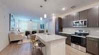 This single-floor, 2-bedroom, 2-bathroom residence is designed for functional everyday living with a clean, modern aesthetic throughout. The open-concept kitchen and living area forms the heart of the home, featuring a generously sized island with granite countertops, a stainless steel undermount sink, and elegant pendant lighting overhead. Dark espresso cabinetry provides ample storage and contrasts beautifully with the light granite surfaces, while stainless steel appliances complete the well-equipped kitchen. Light wood-look flooring runs throughout, enhancing the bright, airy feel of the space. Crown molding adds a refined architectural detail to both the kitchen and living areas.

The living room is a welcoming retreat, bathed in natural light from multiple windows fitted with blinds, and accented by a ceiling fan for year-round comfort. The two bedrooms are carpeted for warmth and comfort, each featuring windows that allow natural light to fill the room. The primary bedroom is a spacious retreat with its own walk-in closet outfitted with wire shelving for organized storage. Both bathrooms mirror the home's modern design language, offering granite-topped vanities with dark wood cabinetry and wood-look tile flooring. This residence combines practical design with contemporary finishes throughout.