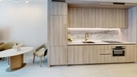 Located on the 38th floor at 77 SE 5th Street in Miami's vibrant Brickell district, this two-bedroom, one-bathroom residence offers a thoughtfully designed layout with high-end finishes throughout. The galley-style kitchen is a standout feature, showcasing light wood cabinetry with brushed gold hardware, a striking marble backsplash, white quartz countertops, and an undermount sink with a sleek gold faucet — all set against light-toned tile flooring that flows seamlessly through the space. The open design allows the kitchen to connect naturally to the living and dining areas, creating an efficient and elegant flow. The spacious primary bedroom is a serene retreat, dressed in warm neutral tones with textured wall coverings, light wood flooring, and ample room for a sitting area. A second bedroom offers flexibility for guests or a home office. The bathroom features floor-to-ceiling stone-tiled walls, a soaking tub with glass enclosure, and gold-accented fixtures that echo the refined aesthetic found throughout. A private balcony with glass railings provides sweeping views of the Miami skyline, offering an ideal outdoor retreat. Recessed lighting, clean white walls, and a cohesive warm-neutral palette give the entire residence a bright, modern, and inviting ambiance.