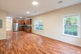 Located at 88 Charley's Place in Bay Shore, NY, this single-floor unit offers a well-designed, open-concept layout that seamlessly connects the living area and kitchen. The living space is finished with warm hardwood-style flooring that reflects recessed lighting overhead, contributing to a bright and welcoming atmosphere. Multiple windows along the exterior walls allow natural light to filter in, offering views of surrounding greenery.

The kitchen is well-appointed with rich medium-toned wood cabinetry, dark countertops, and a full suite of stainless steel appliances, including a refrigerator, gas range with overhead ventilation, and dishwasher. Ample upper and lower cabinet storage makes this kitchen both functional and visually cohesive.

The bedrooms feature neutral wall tones and plush carpeting, with windows framing outdoor tree views that enhance a calm, residential feel. At least one bedroom includes access to a closet with built-in shelving. The bathroom presents a clean, understated design with a wood-toned vanity, white countertop, large mirror, and tile flooring. An electrical panel is conveniently located near the entry area. Overall, the space offers a practical and comfortable single-level living environment.