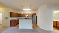 Located at 1100 Deer Harbor Dr in Garner, NC, this well-appointed single-floor residence offers a functional and comfortable layout designed for everyday living. The kitchen serves as a central highlight, featuring warm honey-toned cabinetry, granite countertops, and a full suite of stainless steel appliances including a range, over-the-range microwave, and refrigerator. A peninsula with pendant lighting above provides additional prep space and casual seating, while light hardwood flooring ties the kitchen together seamlessly. The bedrooms are carpeted and generously sized, each equipped with ceiling fans and windows with blinds that allow natural light and outdoor views of the surrounding greenery. The primary bathroom features a wide dual-sink vanity with a marble-style countertop and warm wood cabinetry, while a secondary bathroom includes a combination tub and shower with wood-look flooring and a single vanity. A dedicated laundry room houses full-size side-by-side washer and dryer units with overhead wire shelving for added storage. Throughout the residence, neutral wall tones and clean finishes create a bright, cohesive atmosphere that is both practical and inviting.